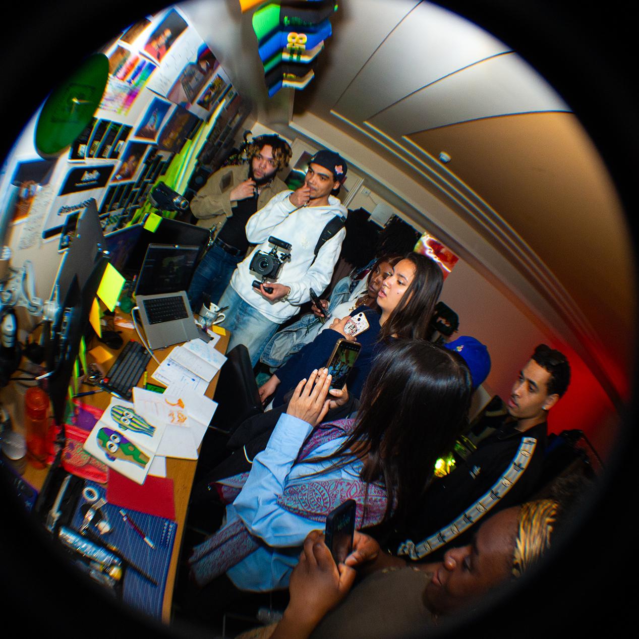 Room installation view using fish eye lens showing people gathered around a desk with screens.