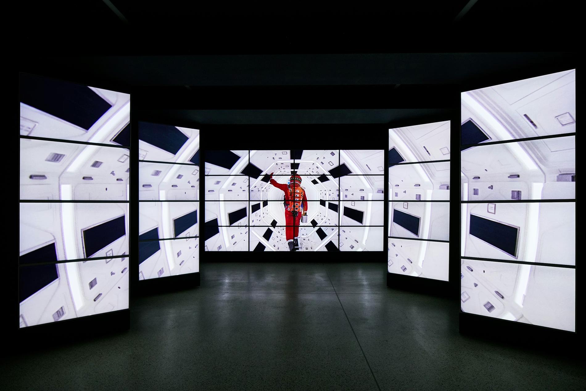 Image of screens showing the film 2001 – an astronaut in orange walks down an illuminated white tunnel