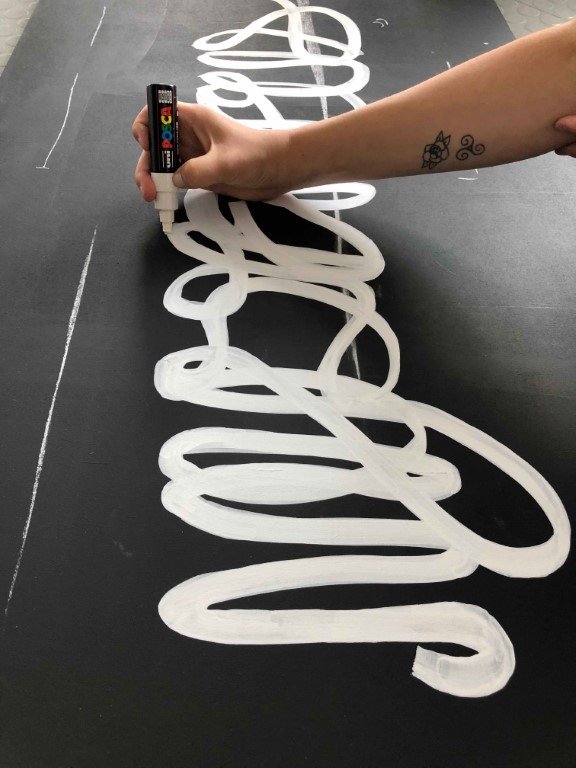 In progress drawing a sign with a white posca pen and swirling letters on a black background