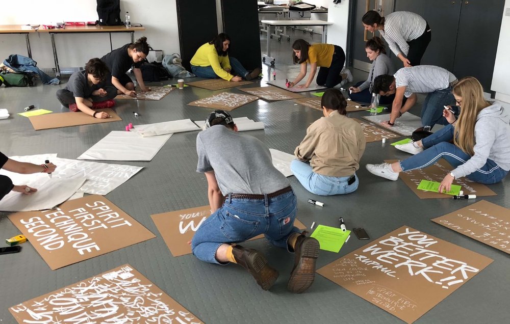 A group of students signpainting on a grey classroom floor during the workshop