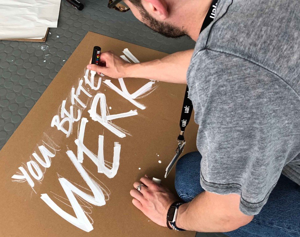 In progress drawing of phrase "you better werk" with white text on cardboard